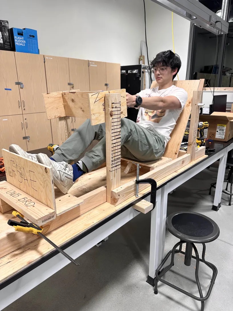 A person sitting in a wooden race car structure.