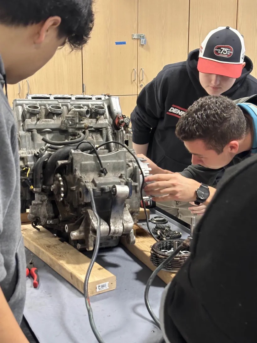 Three people working on an engine at a table.