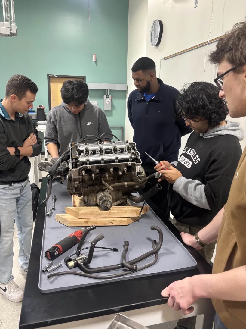 Five people standing around a table working on an engine.