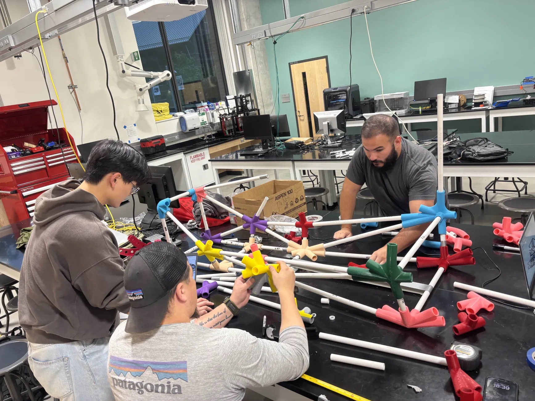 Three students assembling a structure of a formula race car out of pipes.