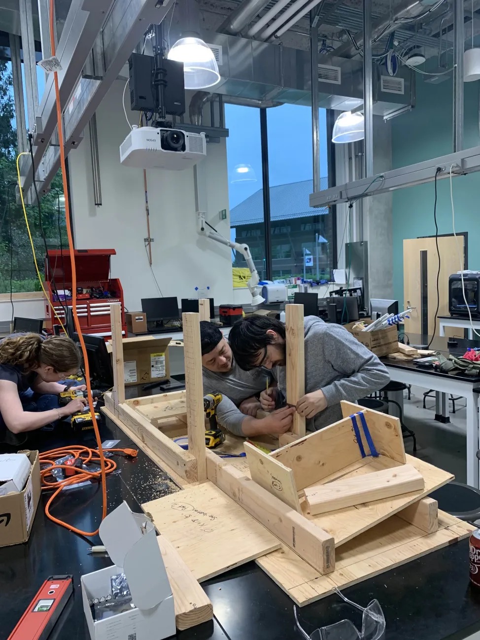 Three people assembling a wooden race car structure.